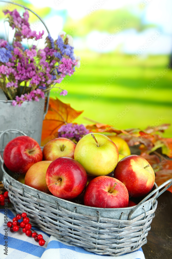 Juicy apples in basket on table on natural background