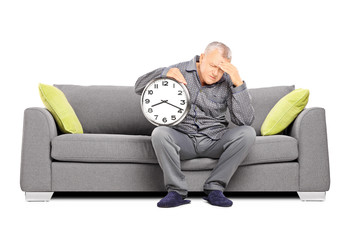 Wall Mural - Mature man in pajamas holding a clock and having a headache