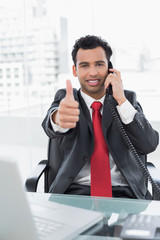 Wall Mural - Businessman gesturing thumbs up while on call at office desk