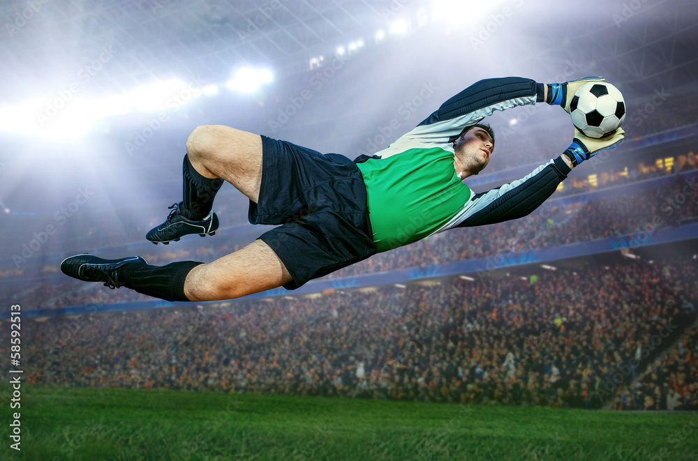 вратарь в прыжке пытается достать мяч в пустом стадионе