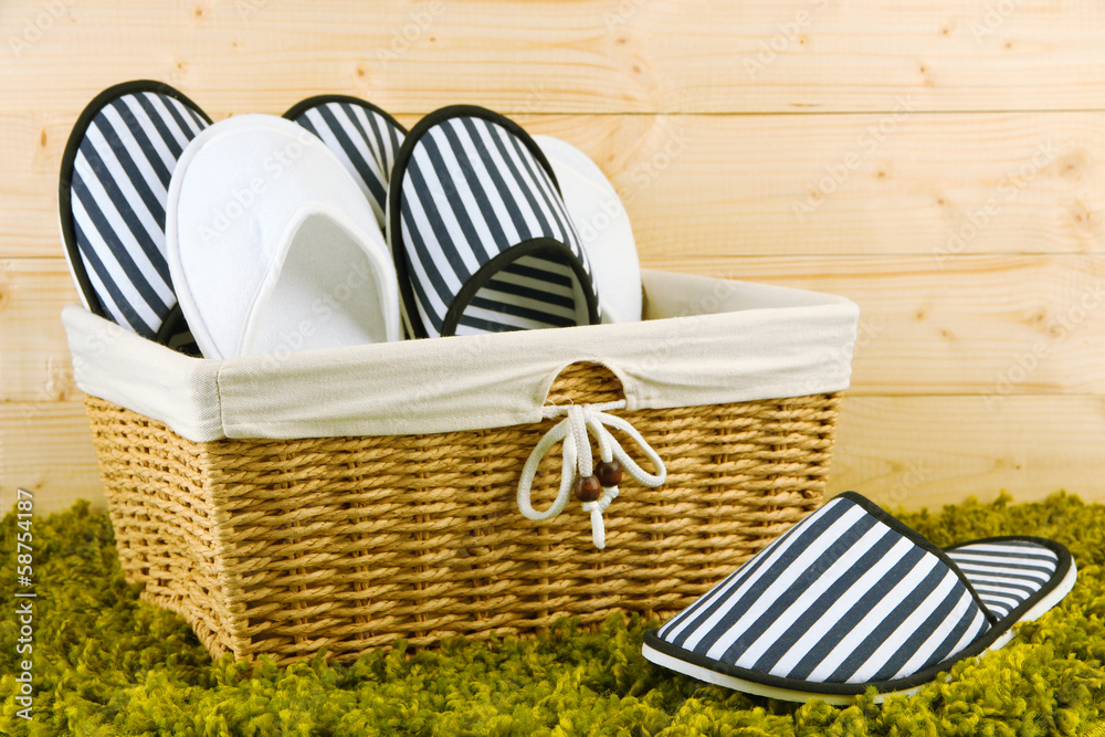 Slippers in basket on carpet on wooden background
