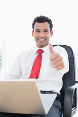 Wall Mural - Smiling businessman with laptop gesturing thumbs up