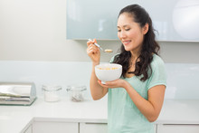 Smiling Young Woman Eating Cereals In Kitchen