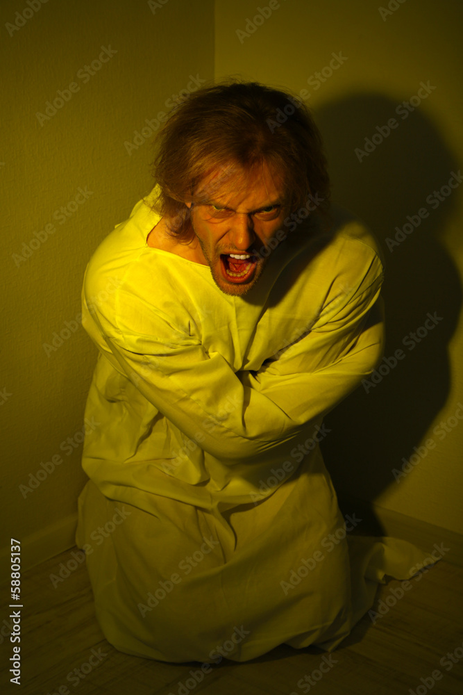 Mentally ill man in strait-jacket in room corner