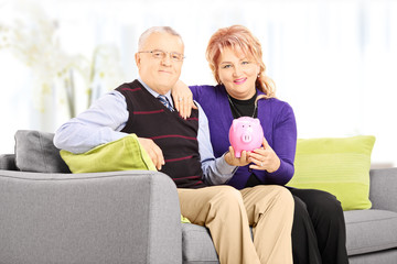 Wall Mural - mature man and woman on sofa holding a piggy bank at home