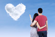© Creativa Images - Young couple pointing at heart clouds