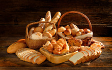 Variety Of Bread In Wicker Basket On Old Wooden Background.