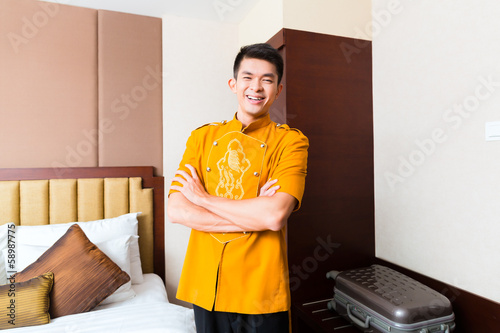 Fotografie, Obraz Asian Chinese porter bringing suitcase to luxury hotel room