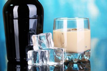 Baileys liqueur in bottle and glass on blue background