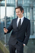 © mimagephotos - Smiling businessman looking at mobile phone outdoors