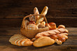 Variety of bread in wicker basket on old wooden background.