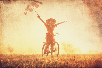 Girl with umbrella on a bike in the countryside in sunrise time