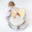 Newborn baby sleeping in a swing on a sheepskin with his sister