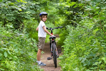 Cute school boy riding a bike in a beautiful summer park