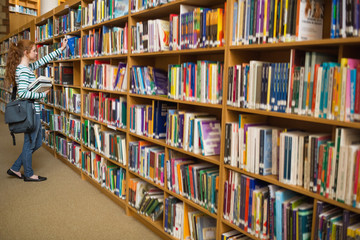 Redhead student taking a book from library bookshelf