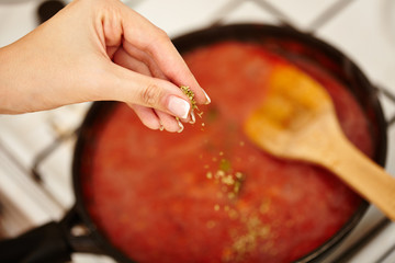 Cook's hand sprinkling parsley and basil in the sauce pan