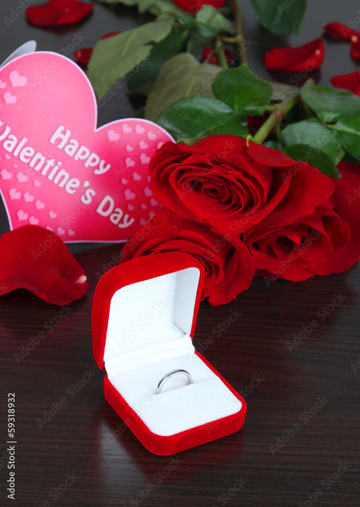 Ring surrounded by roses and petals on wooden table close-up