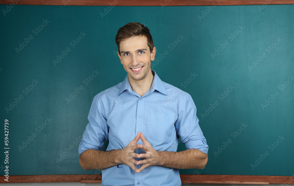 Young teacher near chalkboard in school classroom