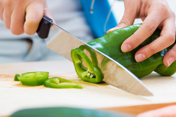 Woman hand cutting a green pepper in kitchen