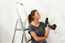 Young Beautiful Brunette Woman Sitting On A Ladder With A Drill