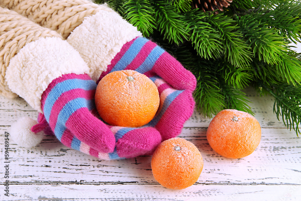 Hands in mittens holding tangerine on wooden background