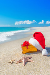 Poster - Santa Claus hat and christmas gift box on the seashore with sea