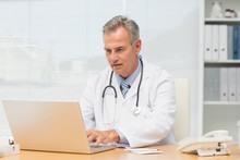 Focused Doctor Sitting At His Desk Using His Laptop