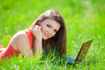 Wall Mural - Portrait of a smart young woman lying on grass and using laptop