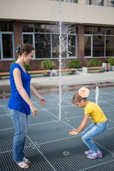 Wall Mural - Mother and daughter having fun standing on grid with fountains