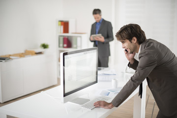 businessman at phone leaning at his computer