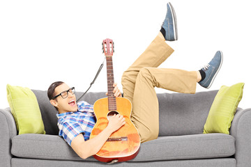 Sticker - Excited young male lying on a modern couch and playing a guitar