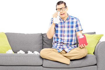 Wall Mural - Sad guy sitting on a sofa and wiping his eyes from crying