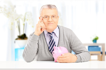 Poster - Senior gentleman posing on a table with piggy bank