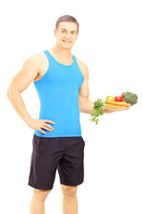 Wall Mural - Young male athlete holding a dish full of fresh vegetables