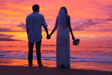Wall Mural - Just married couple holding hands on the beach at sunset