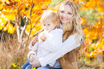 Young mother playing with her daughter in autumn park