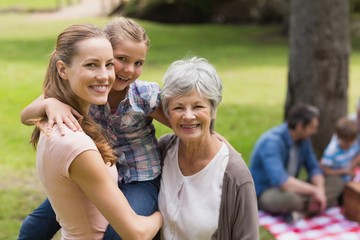 Grandmother, mother and daughter with family in background at pa