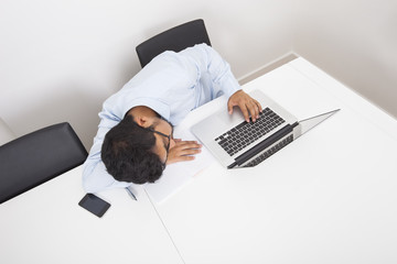 High angle view of businessman sleeping by laptop at desk in office