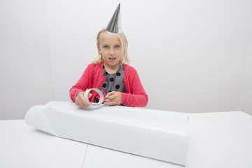 Portrait of cute girl wrapping birthday gift at table in house