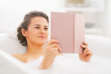 Wall Mural - Happy young woman reading book in bathtub