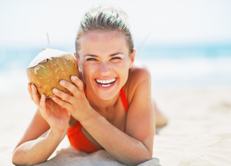 Poster - Portrait of smiling young woman on beach holding coconut