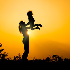 silhouette of a mother and son who play outdoors at sunset backg