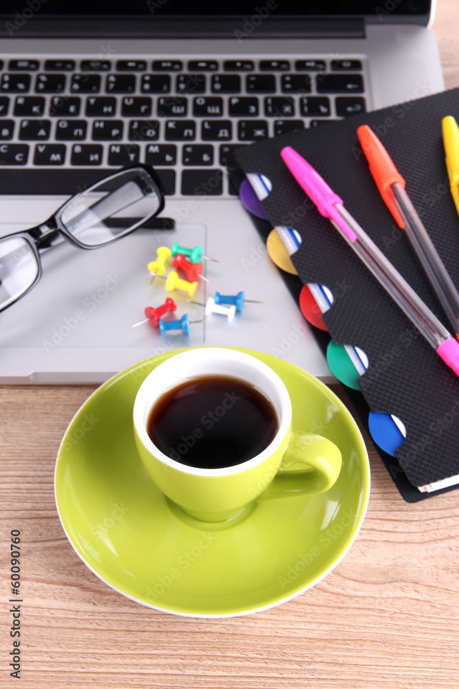 Laptop with stationery and cup of coffee on table