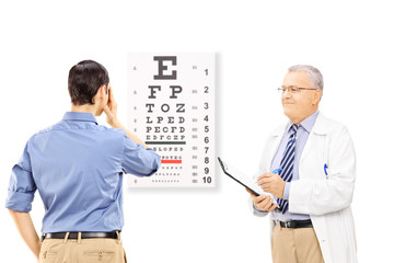 Wall Mural - Young male patient taking eyesight test and an optician holding