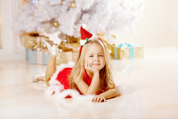 Beautiful little Santa girl near the Christmas tree.  Happy girl