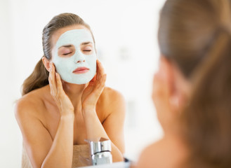 Wall Mural - Young woman applying facial mask in bathroom