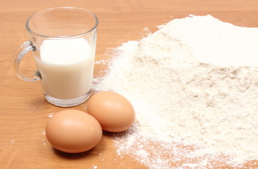 Wheat flour, glass of milk and two eggs on table