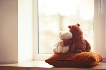 Two embracing teddy bear toys sitting on window-sill