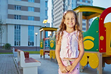 Little girl in pink summer clothes stands at children playground