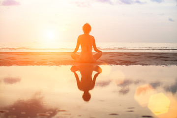 Wall Mural - Yoga woman sitting in lotus pose on the beach during sunset.